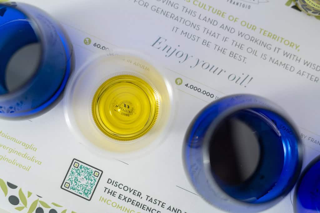 Bicchieri blu da assaggio professionale e olio extravergine dorato su una scheda di degustazione, Frantoio Muraglia
